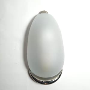 Könnte beinhalten: Eine Wandleuchte aus mattiertem Glas mit abgerundeter, ovaler Form. Die Leuchte hat einen Sockel aus poliertem Chrom und eine kleine, passende Kappe an der Oberseite. Die Leuchte ist für die Wandmontage konzipiert und sorgt für weiches, diffuses Licht.