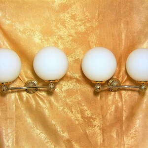 May include: Four white globe light fixtures with gold accents mounted on a silver curved bar.
