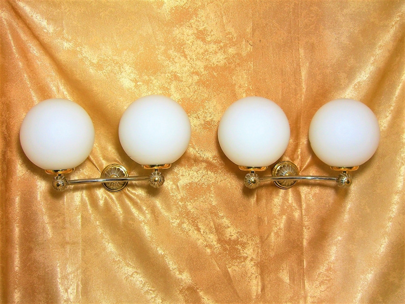 May include: Four white globe light fixtures with gold accents mounted on a silver curved bar.
