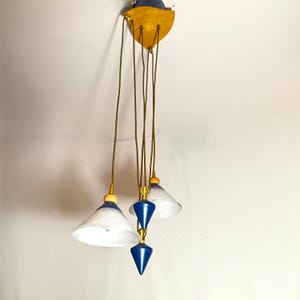 Könnte beinhalten: Eine moderne, mehrflammige Pendelleuchte mit einem Holzbaldachin und drei weißen und blauen Glasschirmen. Die Schirme sind an Schnüren vom Baldachin abgehängt und haben eine blaue und goldene Oberfläche.