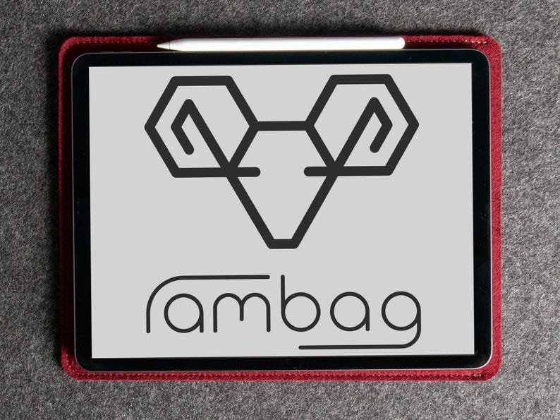 Puede incluir: Una tableta con un gr&aacute;fico de carnero negro y la palabra "rambag" en una fuente redondeada. La tableta est&aacute; en una funda roja y un l&aacute;piz &oacute;ptico blanco descansa encima. El fondo es una superficie gris texturizada.