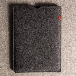 May include: A dark grey felt tablet sleeve with a small, rounded, reddish-brown accent on the right side. The sleeve is rectangular with a slightly curved top edge. The background is a lighter grey felt.