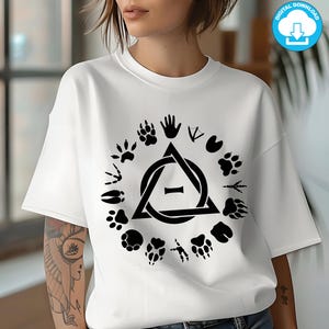 Può includere: T-shirt bianca con un design nero circolare di impronte di animali e un'impronta di mano che circonda un triangolo con una forma di osso all'interno. La maglietta è un download digitale.