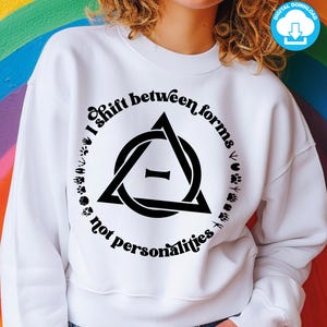 May include: White sweatshirt with a black graphic design featuring a triangle with a line through it and the text "I shift between forms not personalities".