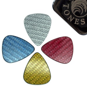 Könnte beinhalten: Vier Gitarrenplektren in Blau, Silber, Rot und Gold, kreisförmig angeordnet. Jedes Plektrum hat eine gewebte Textur. Eine schwarze Hülle mit dem Text "TONES" befindet sich in der oberen rechten Ecke.