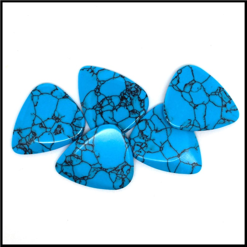 This image show 5 Blue Dragon Skin Reconstituted Stone Guitar Picks. These plectrums have black veins running through a blue background. They are randomly arranged on a white back ground so you can see the 3D shape of their design.