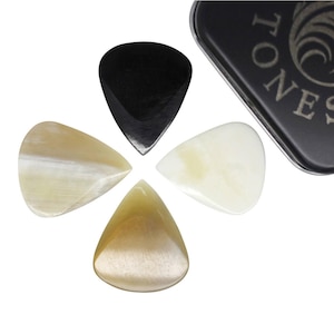 May include: Four guitar plectrums in a variety of colours, including black, cream, and tan, arranged in a circular pattern. A black metal case with the word "TONES" is visible. The plectrums have a smooth, polished appearance.