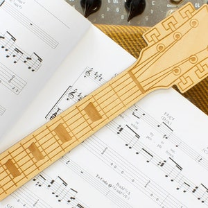May include: A wooden guitar-shaped bookmark with a fretboard and headstock design. The bookmark is lying on a sheet of music with musical notes and chords.