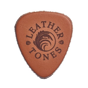 May include: A brown leather guitar pick with the words "Leather Tones" and a stylized leaf design.