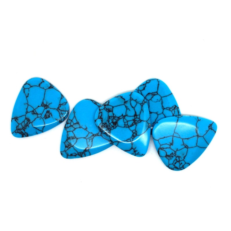 This image show 5 Blue Dragon Skin Reconstituted Stone Guitar Picks. These plectrums have black veins running through a blue background. They are randomly arranged on a white back ground so you can see the 3D shape of their design.