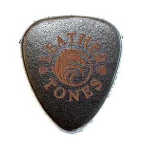 May include: A black leather guitar pick with the words "Leather Tones" and a logo of a stylized wave in a circle, all in brown.