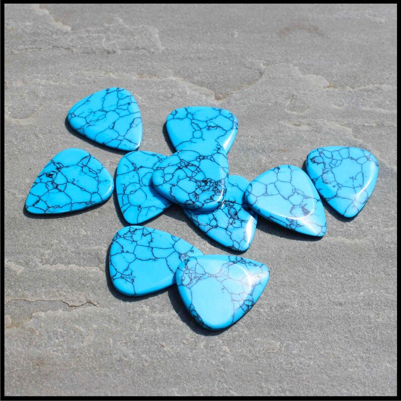 This image show 5 Blue Dragon Skin Reconstituted Stone Guitar Picks. These plectrums have black veins running through a blue background. They are randomly arranged on a stone back ground so you can see the 3D shape of their design.