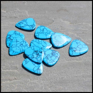 This image show 5 Blue Dragon Skin Reconstituted Stone Guitar Picks. These plectrums have black veins running through a blue background. They are randomly arranged on a stone back ground so you can see the 3D shape of their design.