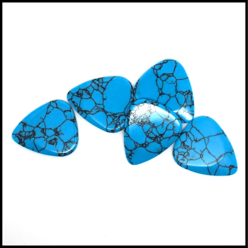 This image show 5 Blue Dragon Skin Reconstituted Stone Guitar Picks. These plectrums have black veins running through a blue background. They are randomly arranged on a white back ground so you can see the 3D shape of their design.