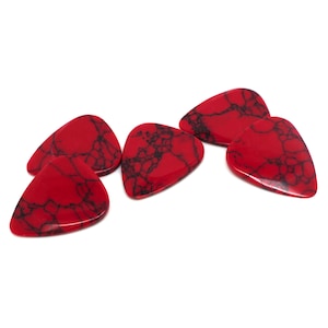 May include: Five red guitar picks with black marbling. The picks are shaped like a teardrop.