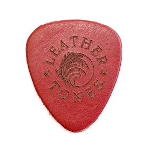 May include: A red leather guitar pick with the words "Leather Tones" and a stylized logo of a wave and feather design.