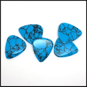 This image show 5 Blue Dragon Skin Reconstituted Stone Guitar Picks. These plectrums have black veins running through a blue background. They are randomly arranged on a white back ground so you can see the 3D shape of their design.