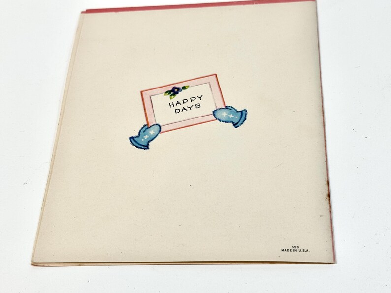 May include: A vintage greeting card with a cream-colored background and a pink border. The card features a rectangular frame with the words "HAPPY DAYS" and two blue mitten illustrations. The bottom right corner reads "MADE IN U.S.A."
