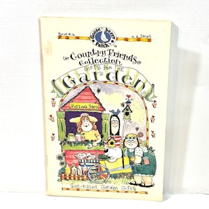 Puede incluir: Un libro vintage titulado "The Country Friends Collection: Gifts from the Garden". La portada presenta una colorida ilustración de un cobertizo de macetas, personajes y una carretilla. El libro es de la serie "Gooseberry Patch".