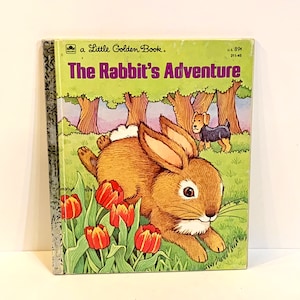 Op de afbeelding: Een Little Golden Book getiteld The Rabbit's Adventure met een bruin konijn in een groen veld met rode en gele tulpen. Een kleine zwart-bruine hond staat op de achtergrond bij bomen. Het boek heeft een grijze rug met een patroon en een witte rand.
