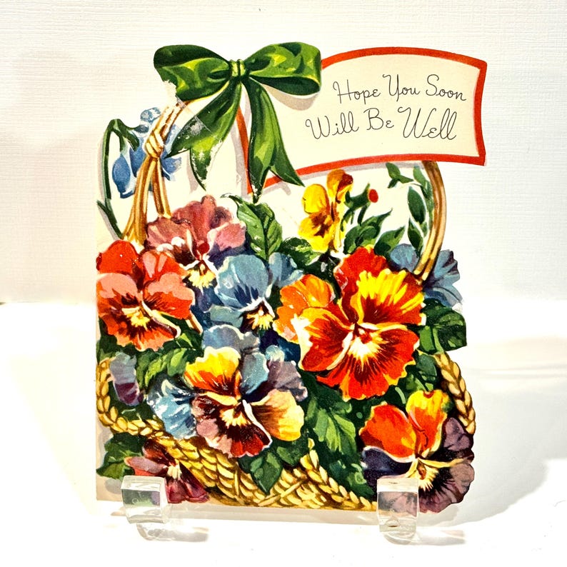 May include: Vintage get-well card featuring a basket overflowing with colorful pansies in shades of red, yellow, orange, and blue. A green bow adorns the top, and a banner reads "Hope You Soon Will Be Well."