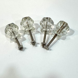 May include: A white ceramic mug with a black handle and the text "But First, Coffee" in a bold, black font. The mug is set against a blurred background, suggesting a cozy setting. The mug appears to be approximately 4 inches tall.