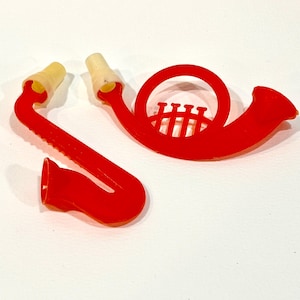 May include: Red plastic musical instrument toys, including a saxophone and a French horn, with yellow mouthpieces. The saxophone is in three pieces. The French horn has a detailed design. These toys are likely for children.