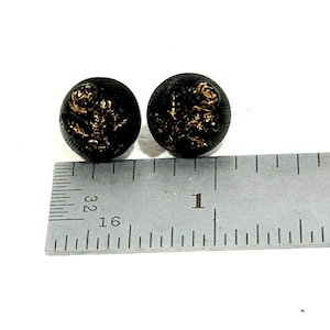 May include: Two black round buttons with gold floral designs. The buttons are approximately 1 inch in diameter. The buttons are set against a white background.
