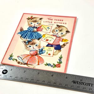 May include: Vintage birthday card featuring three kittens holding signs that read "Happy Birthday to You." The kittens are dressed in blue and red outfits. The card has a pink border and floral accents.