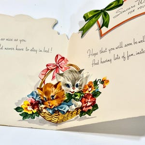 May include: Vintage get-well card featuring two kittens in a woven basket with flowers. The kittens are orange and gray, with blue bows. The card has handwritten text that reads "Anyone so nice as you should never have to stay in bed!" and "Hope that you will soon be well."