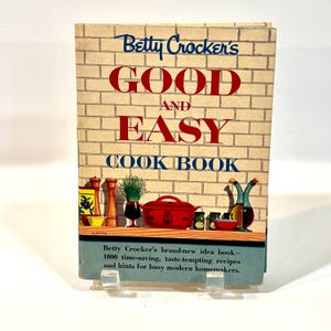 May include: A vintage cookbook titled "Betty Crocker's Good and Easy Cook Book" with a brick-patterned background. The cover features red text and illustrations of kitchen items. The book promises 1000 recipes.