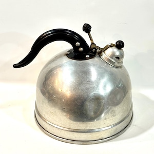 May include: A vintage, silver-toned metal kettle with a black handle and spout. The kettle has a rounded body and a small, round lid with a black knob. The handle is curved and attached to the body with rivets. A classic kitchenware item.
