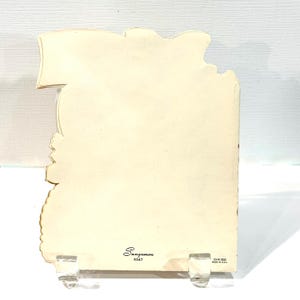 May include: Vintage greeting card with a cream-colored background, held by a clear acrylic stand. The card has a unique shape with a banner-like top and decorative edges. The Sangamon K547 logo is visible.