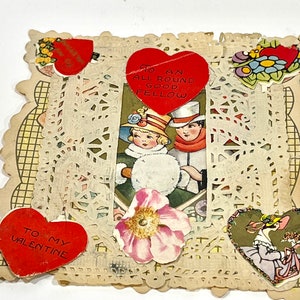 May include: Vintage Valentine's Day card with a central image of a couple in winter attire. The card features red heart-shaped accents with text, floral embellishments, and a decorative lace border. The card is aged with a vintage aesthetic.