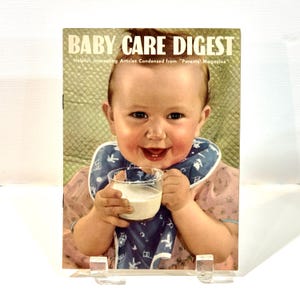 Peut inclure: Couverture de magazine vintage "Baby Care Digest" avec un bébé souriant tenant un verre de lait. Le bébé porte un bavoir bleu avec des illustrations blanches et une robe rose. Le titre du magazine est en lettres blanches en gras.