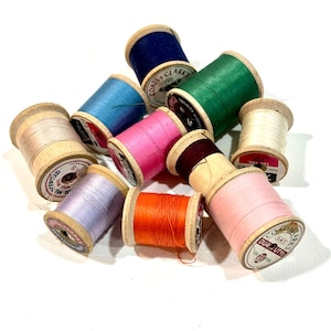 May include: A collection of colorful spools of thread in various shades, including blue, green, pink, and orange. The spools are made of wood and have labels with text. Ideal for sewing and crafting projects.