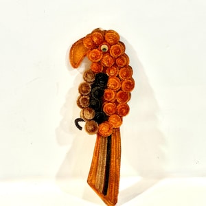 May include: A handcrafted parrot decoration made from orange, brown, and black pipe cleaners. The bird features a detailed beak, eye, and tail, with a textured body. The parrot is a unique, handmade item, perfect for adding a touch of whimsy to any space.