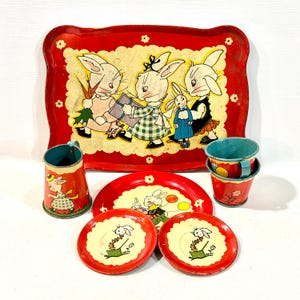 May include: A vintage metal children's tea set featuring red and cream colours with illustrations of rabbits. The set includes a large rectangular serving tray, a pitcher, two cups, a small round plate, and two saucers, all decorated with floral motifs.