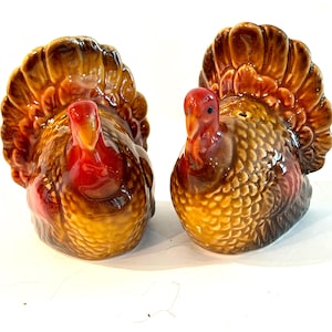 May include: A pair of ceramic salt and pepper shakers shaped like turkeys. Each turkey features a glossy brown and tan finish with a textured feather pattern on the body and a large, fanned tail. The heads are painted in a vibrant red and orange.