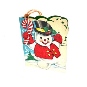 May include: A vintage-style paper gift tag featuring a cheerful snowman wearing a black top hat with holly, a red vest, and red mittens. The snowman holds a red and white striped candy cane against a blue winter background with a green pine tree.