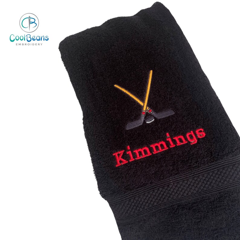 May include: Black bath towel with red embroidery of crossed hockey sticks and a puck, and the name "Kimmings" below.
