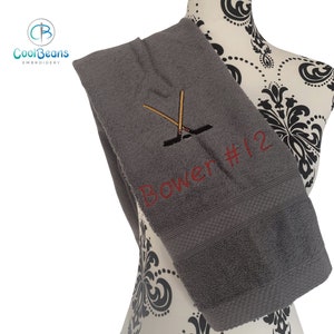 May include: Gray towel with red embroidery of hockey sticks and the text "Bower #12"
