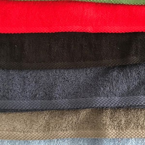 May include: A stack of eight towels in various colors, including pink, green, red, black, blue, gray, light blue, and peach. The peach towel has the name "Luna" embroidered on it.