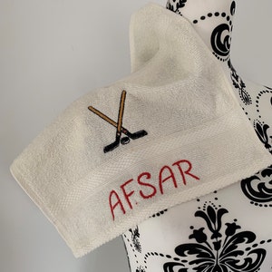 May include: White towel with red embroidery of the name "AFSAR" and a pair of crossed hockey sticks with a puck.