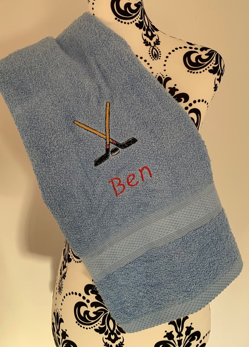 May include: A light blue towel with a personalized embroidered design featuring crossed hockey sticks and the name "Ben".