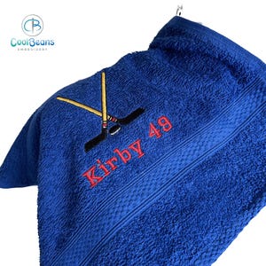 May include: Blue towel with embroidered hockey sticks, a puck, and the name "Kirby 49" in red thread.