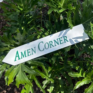 May include: White wooden arrow sign with the words "AMEN CORNER" in green lettering.