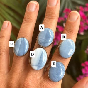 May include: Five rings with oval, light blue gemstones set in silver-colored bands. The gemstones have a marbled appearance with white and blue swirls. The rings are displayed on a hand.
