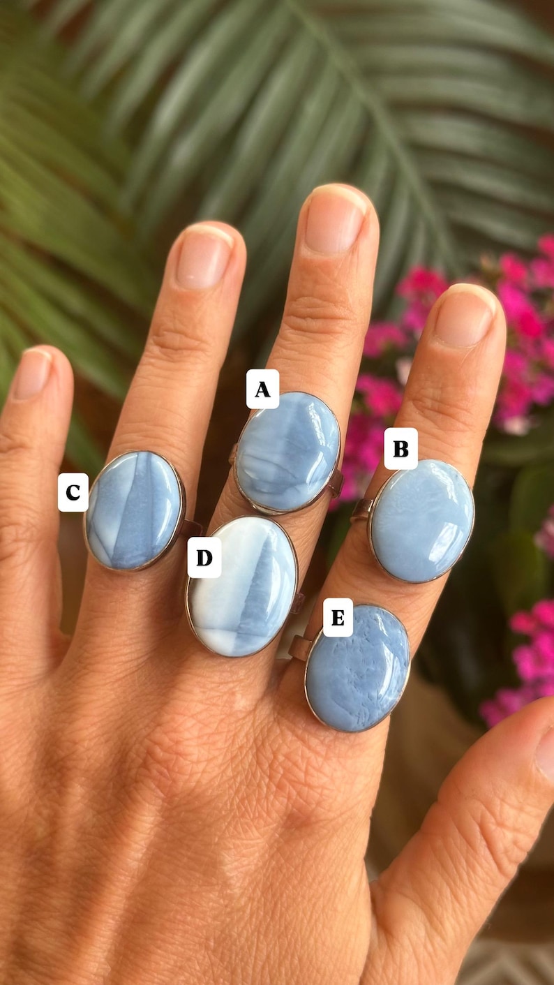May include: Five rings with oval, light blue gemstones set in silver-colored bands. The gemstones have a marbled appearance with white and blue swirls. The rings are displayed on a hand.