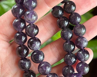 May include: A double-strand bracelet composed of polished, spherical amethyst beads. The beads exhibit deep purple hues with natural variations in colour density and internal marbling, strung together to form a continuous circular loop.